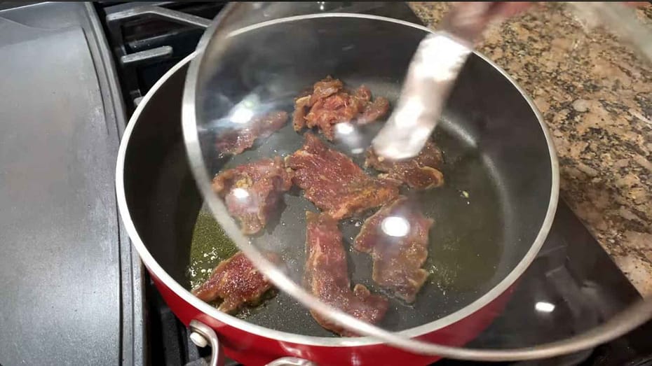 Cooking the marinaded beef tapa with a little oil in a saucepan.