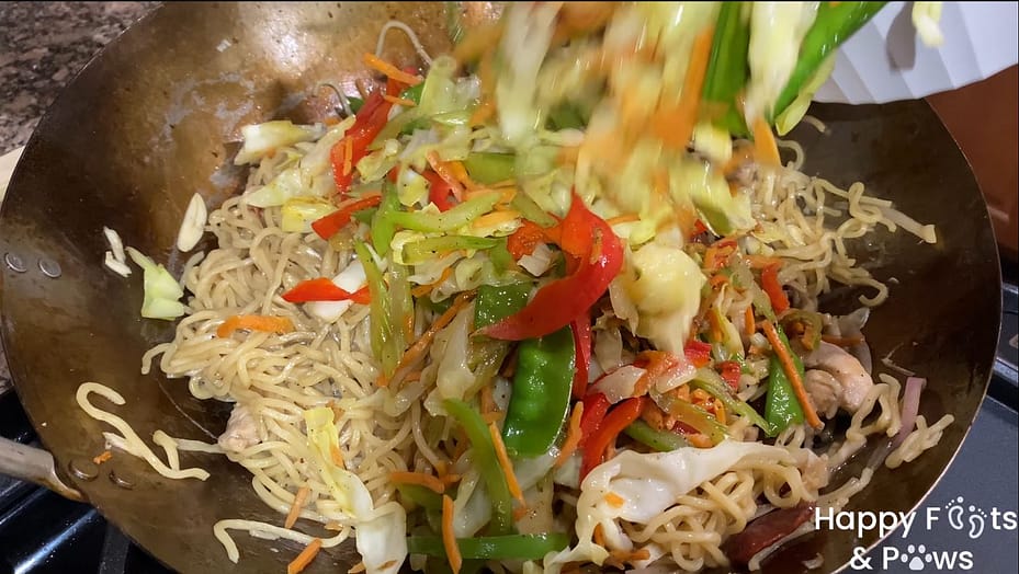 Adding the already cooked vegetables to the cooked noodles and mixing together