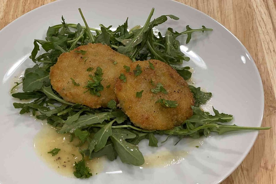Two shrimp cakes on a plate with Beurre Blanc Sauce and arugula greens