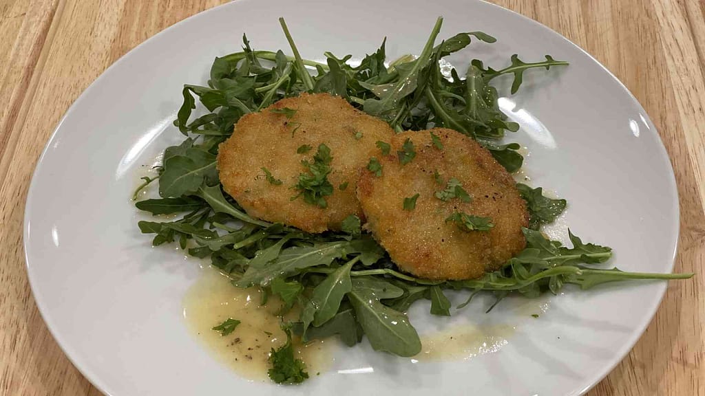 Two shrimp cakes on a plate with Beurre Blanc Sauce and arugula greens
