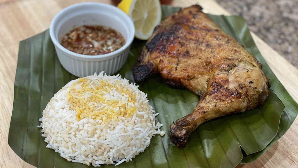 Filipino chicken inasal with rice on a banana leaf with sauce