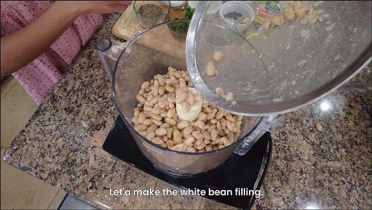 white beans being placed in food processor for white bean ravioli recipe