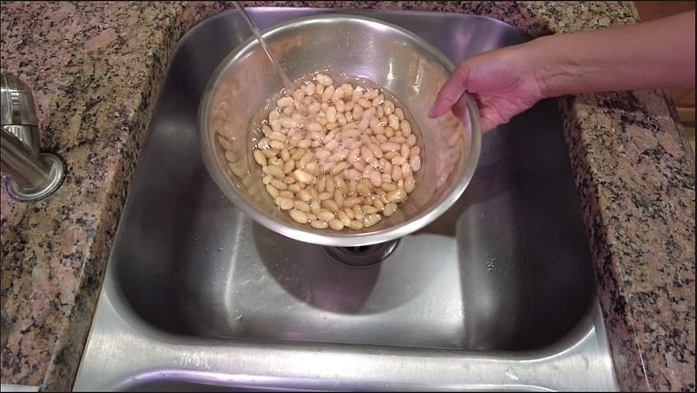 white beans being rinsed in a bowl
