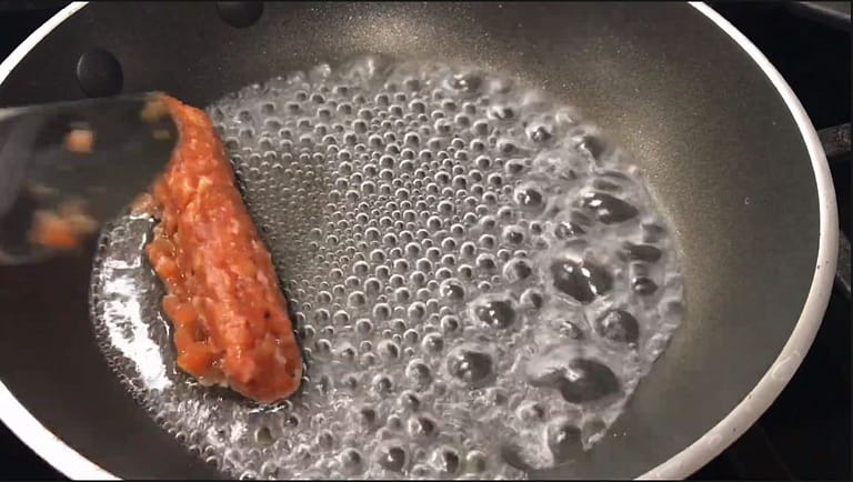 boiling water in a pan with one longanisa being placed inside