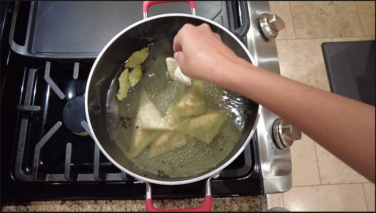 white bean ravioli's being placed in boiling water on stove in a pot