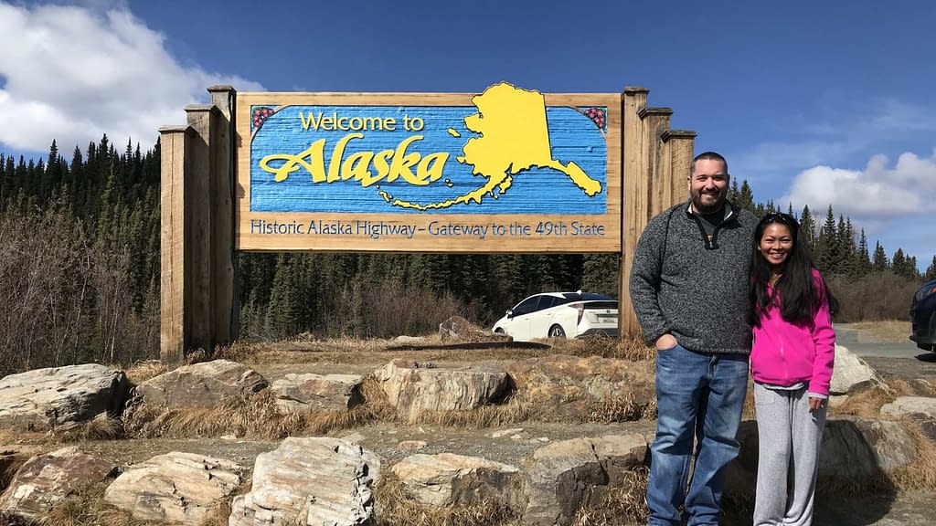 couple standing next to the welcome to alaska sign on the border between the Yukon and Alaska