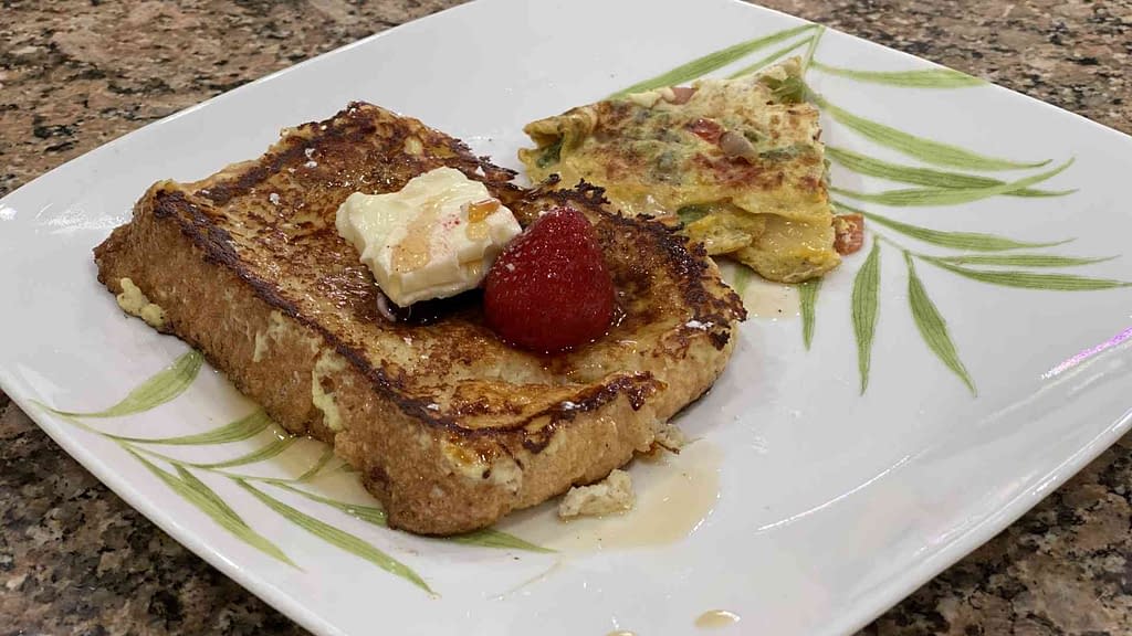 homemade french toast with butter, fruit, maple syrup and omelet on the side