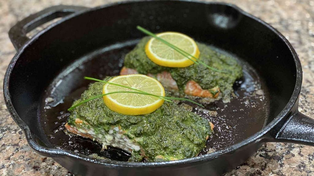Baked salmon pesto on a cast iron pan with lemon slices and spring onions on top