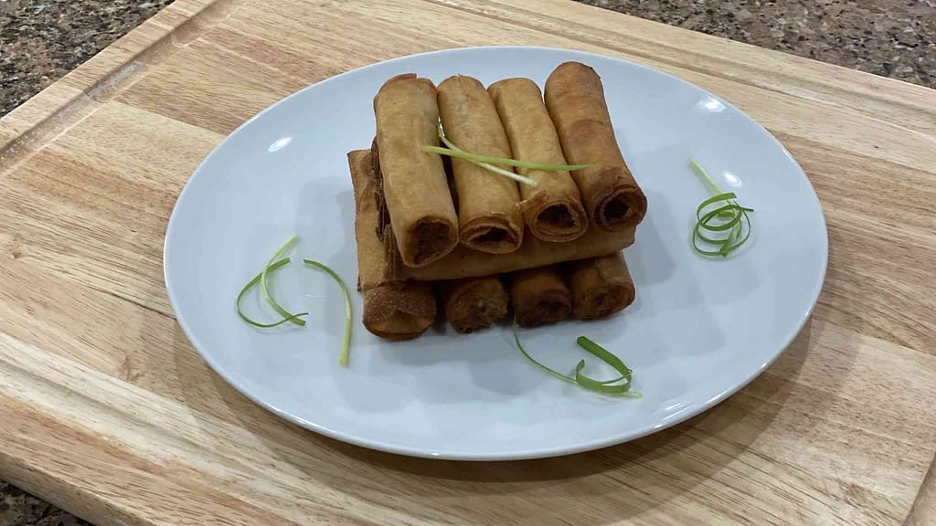 A stack of filipino lumpia shanghai on a plate with spring onions