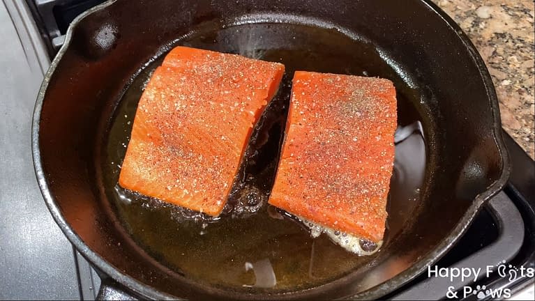 Two sockeye salmon fillets cooking in a cast iron pan with olive oil
