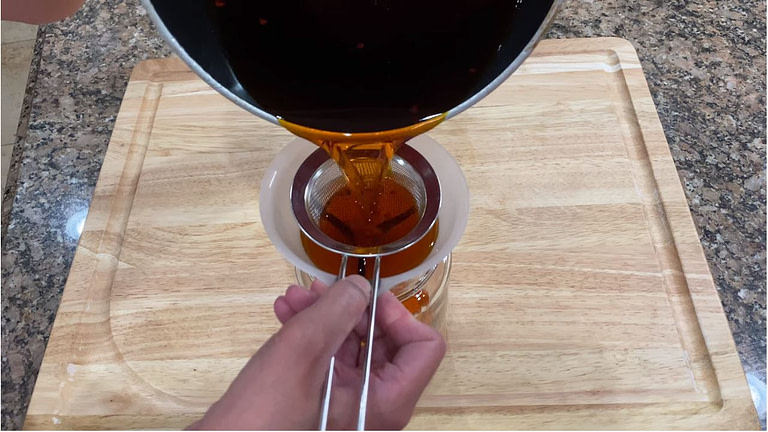 annatto oil being being poured through a strainer and into a funnel for storage