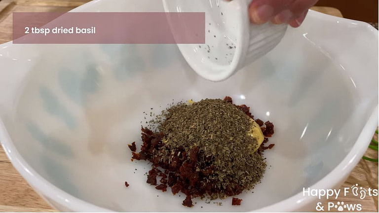 Adding dried basil to sun-dried tomato vinaigrette dressing recipe in bowl