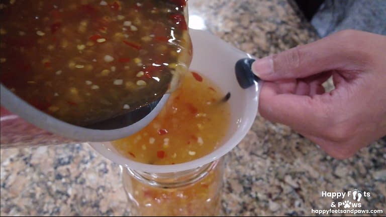 sweet chili sauce being poured into a mason jar via funnel