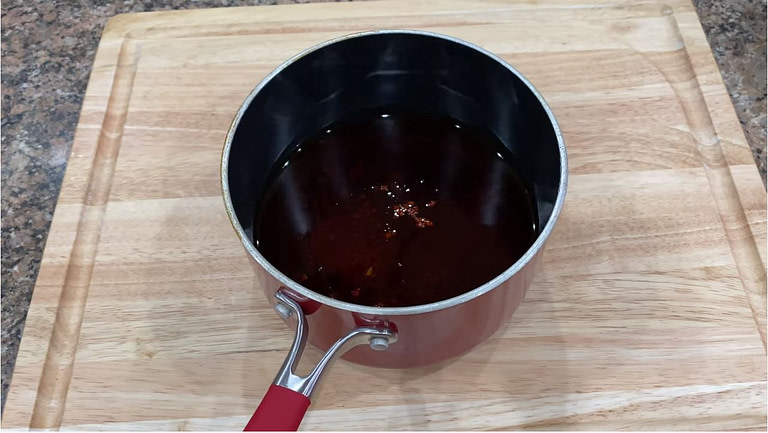 cooked annatto oil cooling in a pot on a wood cutting board