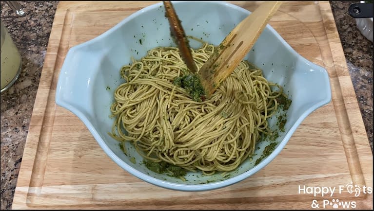 mixing noodles and pesto in a large glass bowl